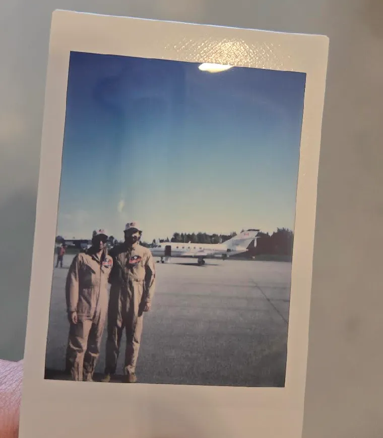 Instant photograph of two CLOT-LESS team members in flight suits beside an aircraft.