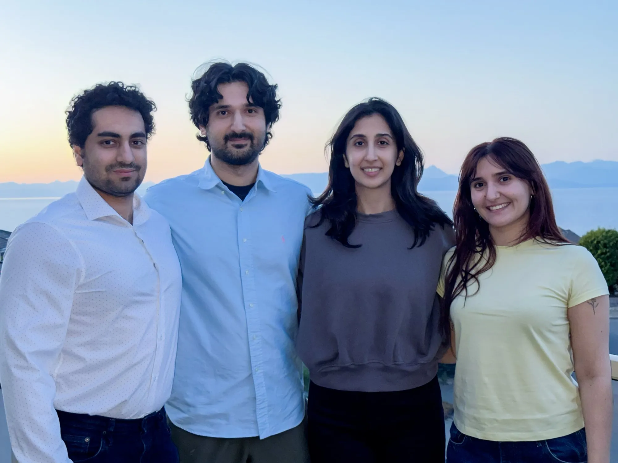 Four members of Team CLOT-LESS standing together outdoors at sunset, with the ocean and mountains behind them.