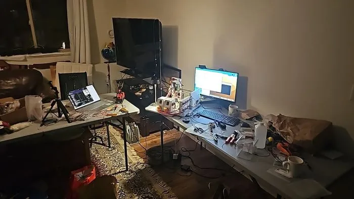 Wide view of the workbench with the payload, monitors and tooling laid out during an evening integration session.
