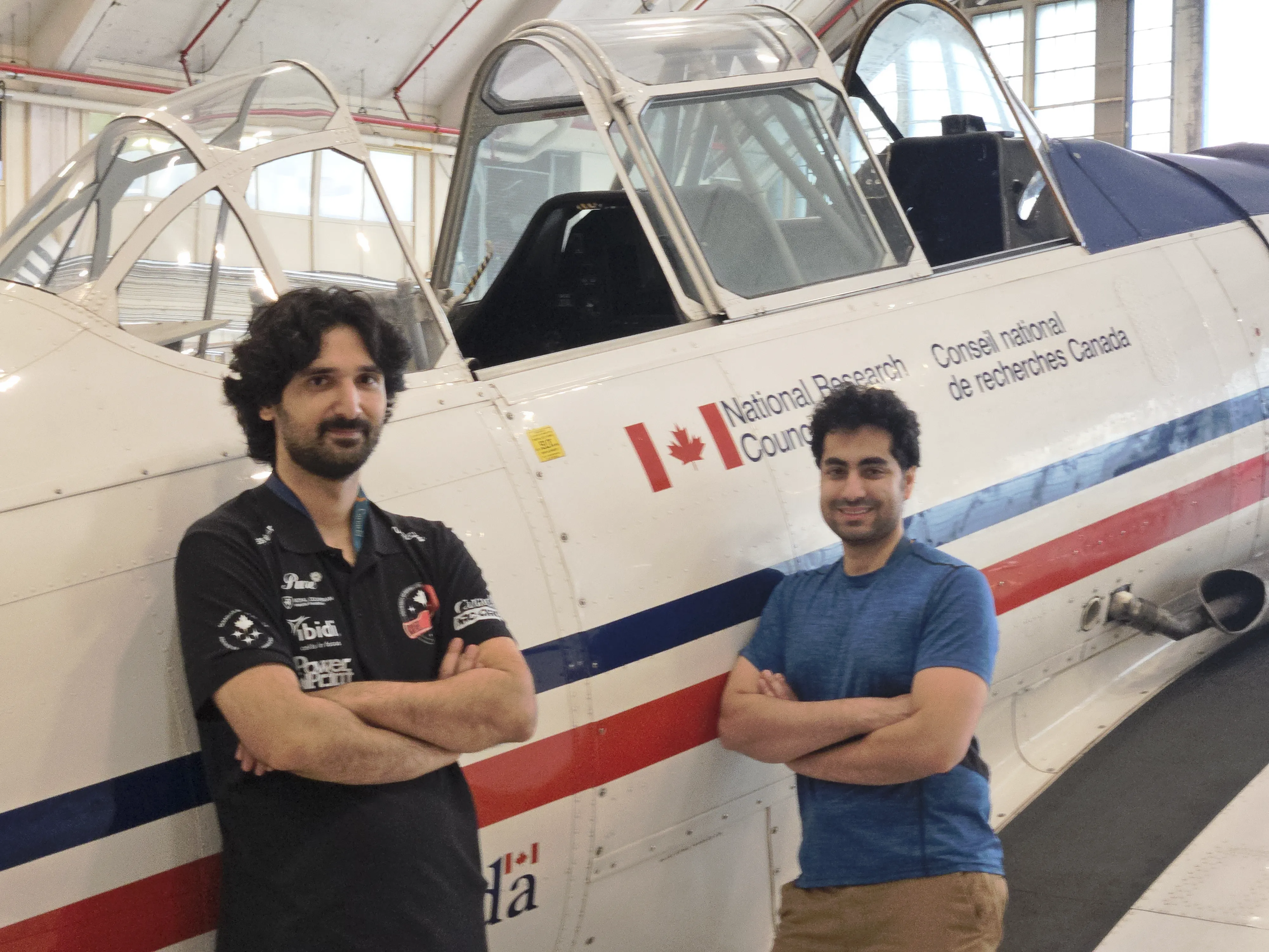 Two CLOT-LESS team members standing beside a National Research Council Canada aircraft in a hangar.